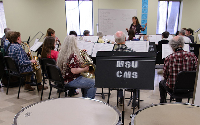 people playing instruments, seated and following lead of director.
